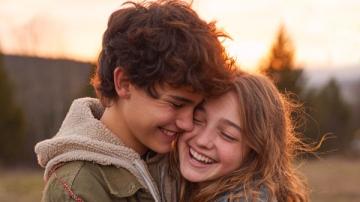 Due adolescenti (un ragazzo e una ragazza) sorridono vicini e con manifesta complicità. Immagine creata con IA